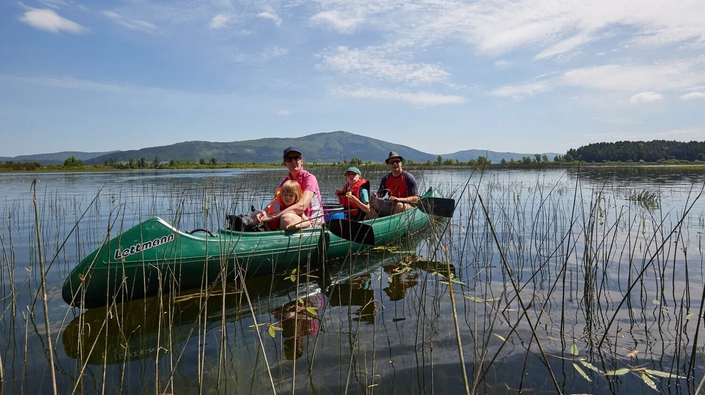 A group of three people in a larger green canoe are rowing on Lake Cerknica, with mount Slivnica visible far in the background.
