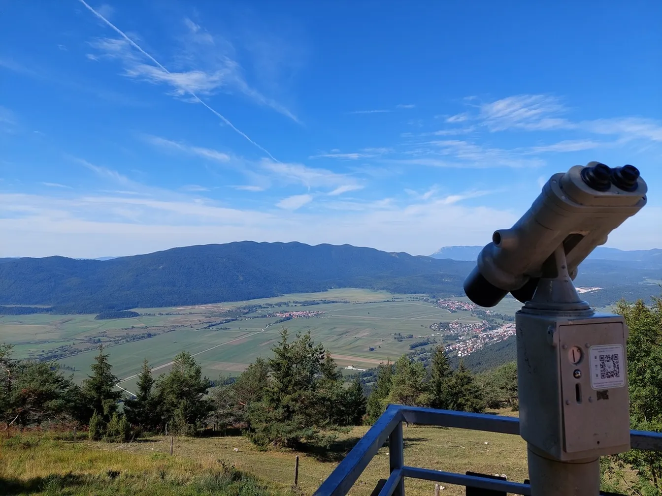 Coprnica cycling trail - Stationary binoculars on Slivnica, with a panorama of Lake Cerknica and the Javorniki mountains in the background. The lake is without water, so the grassy surface dominates.
