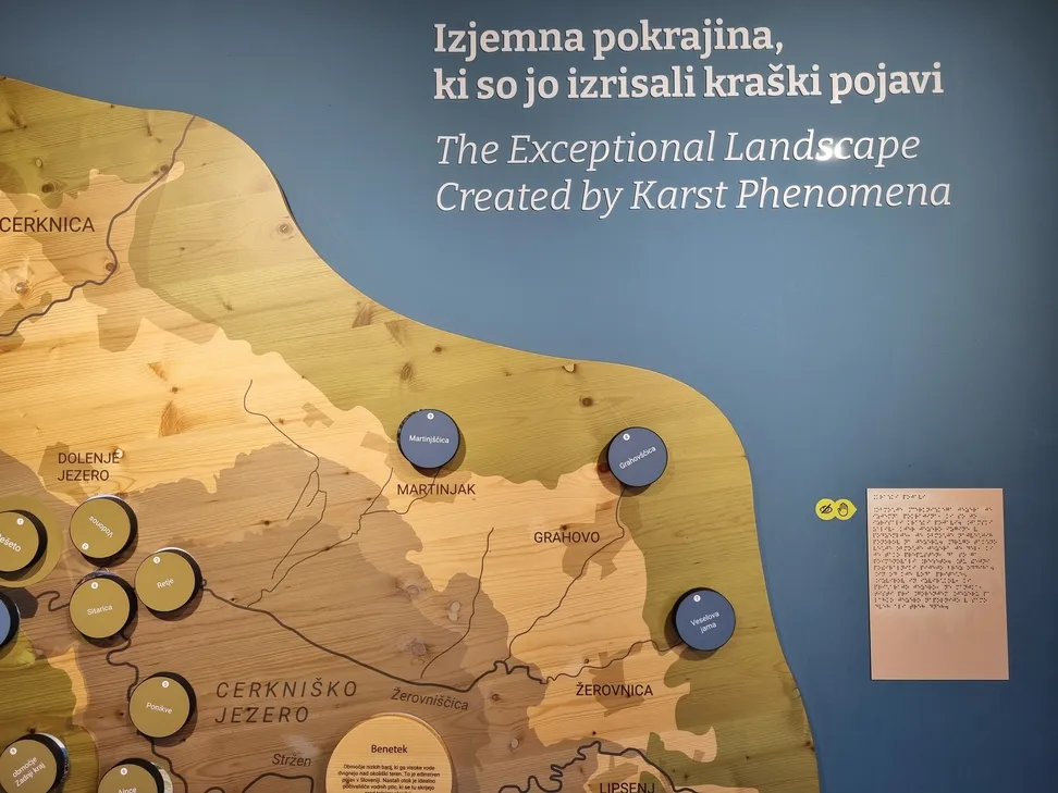Tablica z Braillovo pisavo v Centru za obiskovalce Cerkniško jezero. Poleg zemljevida Cerkniškega jezera je tablica z Braillovo pisavo, namenjena slepim in slabovidnim za lažji dostop do informacij.