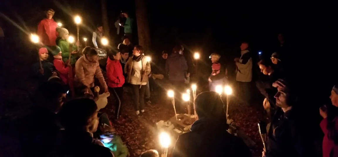 Množica ljudi v mraku, večina jih v rokah drži prižgane bakle, ki razsvetljujejo okolico.