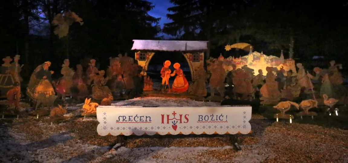 Gasparijeve narodne jaslice v vasi Selšček. V ospredju je Sveta družina. Spredaj je tabla z napisom »Srečen božič« in okrasnimi motivi, v ozadju pa figure pastirjev, živali in drugih likov.