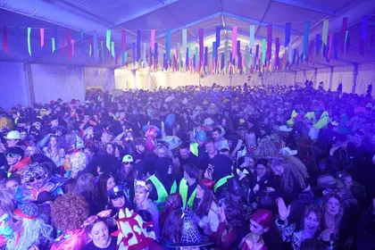 A crowd of visitors in masks at a carnival party in Cerknica under a marquee. The tent is decorated with hanging ribbons, as is customary for the Cerknica carnival.