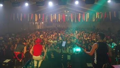 A musical group on stage under a marquee, in front of them a crowd of visitors at a carnival party. The tent is decorated with hanging ribbons, as is customary for the Cerknica carnival.