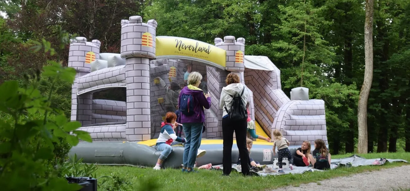 Children play on an inflatable castle while parents watch nearby in the park.