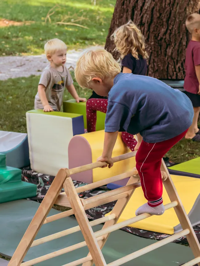 A child climbs a wooden play structure in an outdoor activity area for young children.