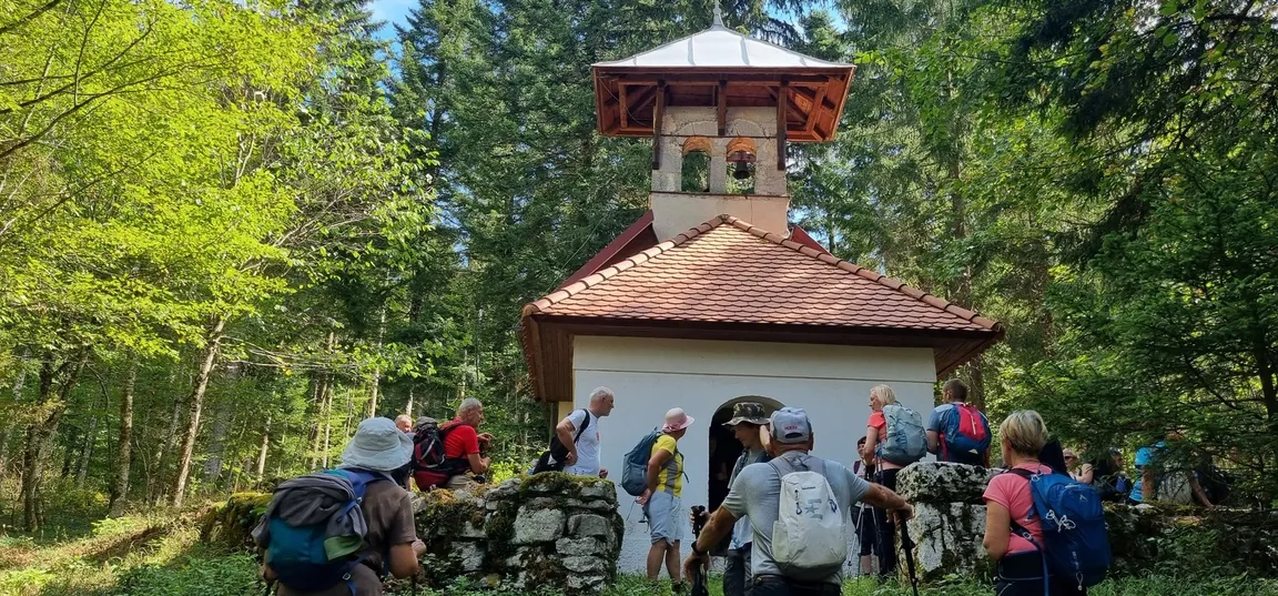 Hikers gathered by a small chapel in the forest.