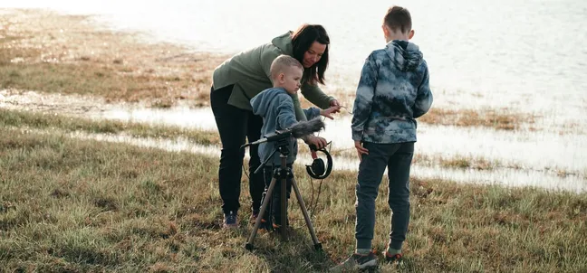 Družina ob jezeru snema zvoke narave med zvočnim sprehodom v Notranjskem parku.