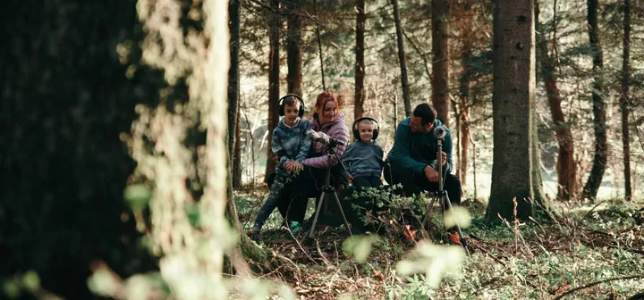 Družina posluša zvoke narave na zvočnem sprehodu v Notranjskem parku.