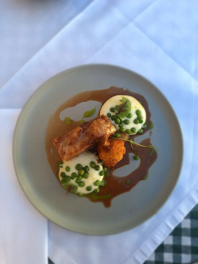 Jed z mesom, pire krompirjem, grahom in omako, postrežena na belem prtu z mikro zelenjem