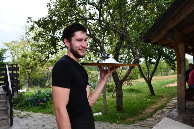 Oseba drži pladenj s pokrito jedjo na prostem, v vrtu ali parku.