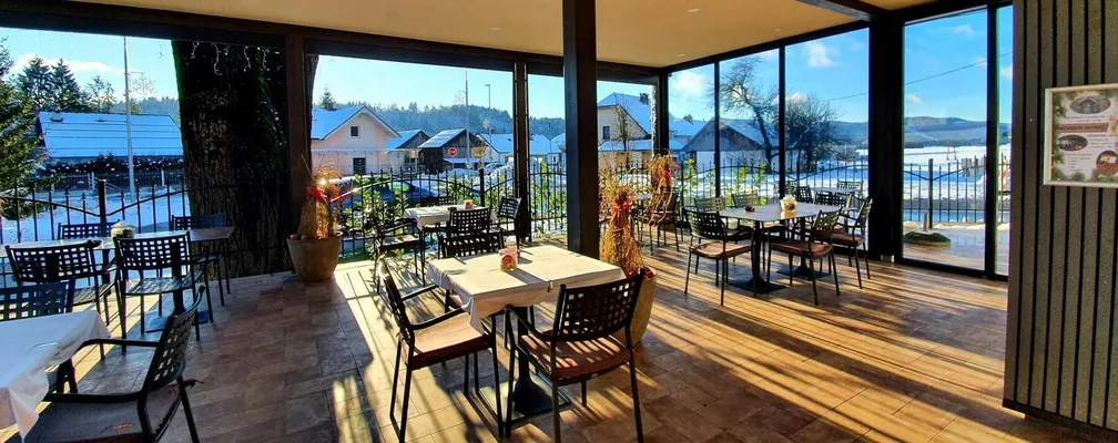 Zunanja terasa restavracija obsijana s soncem. V ozadju so hiše z zasneženimi strehami.