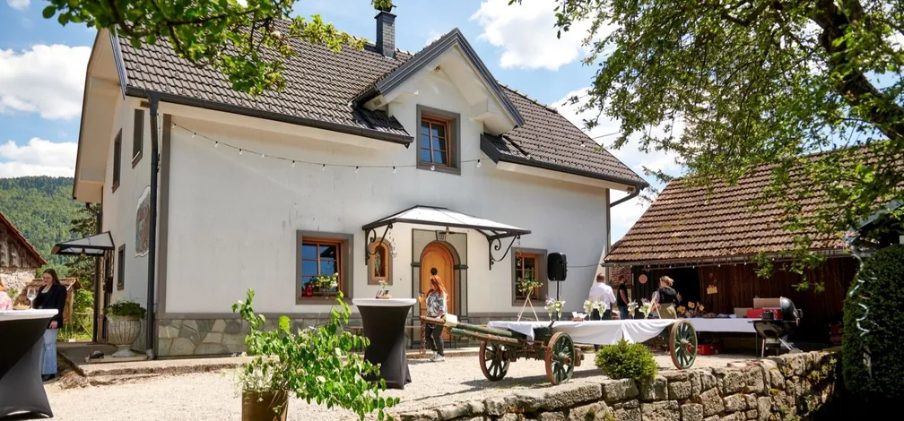 Bela hiša posestva Bajer s cvetličnimi okni in mizami, pripravljenimi za dogodek na prostem