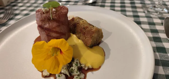 Gourmet dish at Notranjska House – bacon-wrapped meat, herbs, and sauce on an elegant plate.