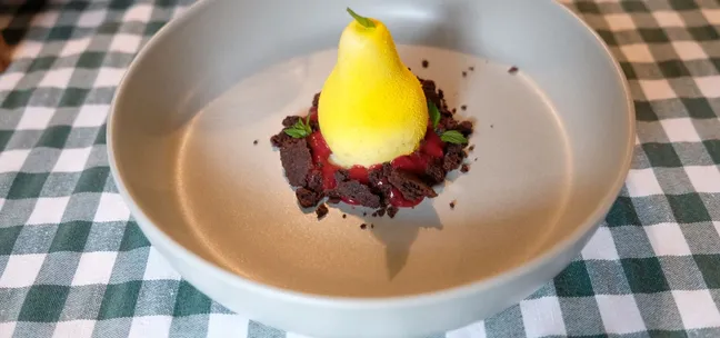 Pear-shaped dessert at Notranjska House – yellow mousse pear on chocolate crumbles with red sauce and herb garnish.