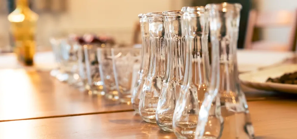 A row of tasting glasses for spirits on a wooden table.