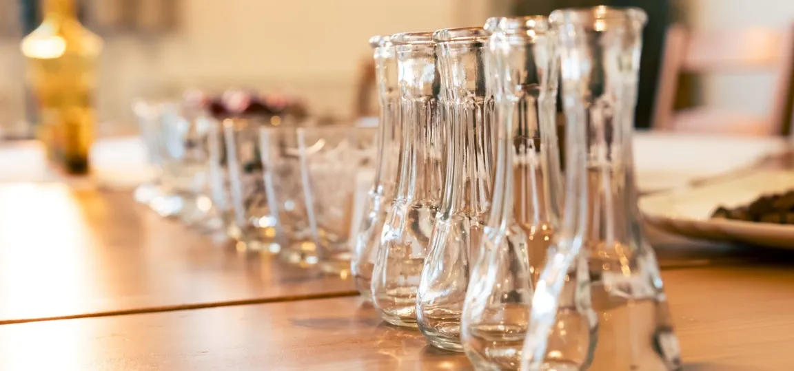 A row of tasting glasses for spirits on a wooden table.