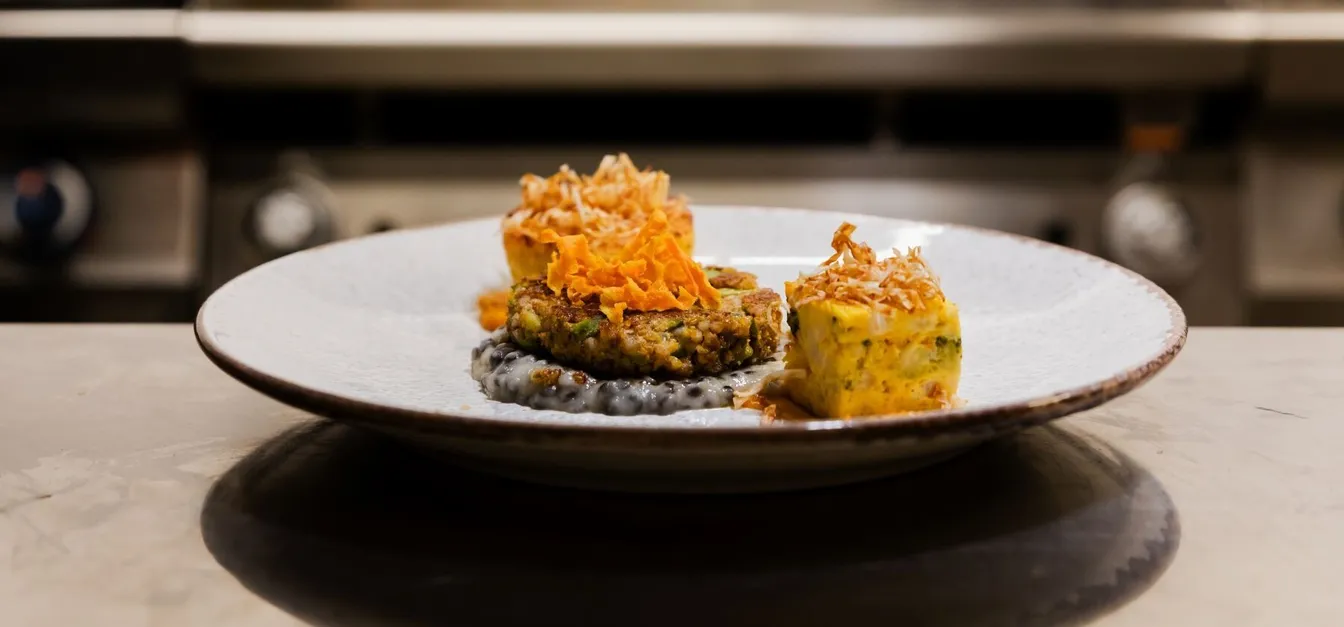 Vegetarian main course at Gostilnica Domin, buckwheat patty with broad beans and lentils, light potato risotto, celery root puree with black lentils, roasted vegetable reduction with apple cider vinegar and honey, beetroot cream on a round white plate on the counter.