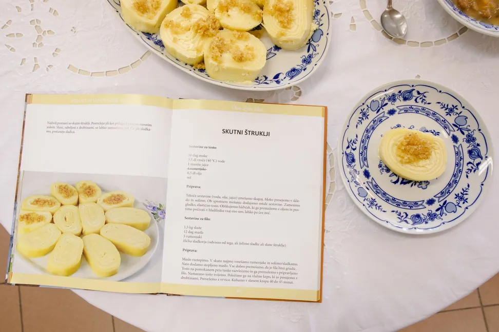 Cottage cheese štruklji on a round table covered with a white tablecloth, next to an open book with recipes.