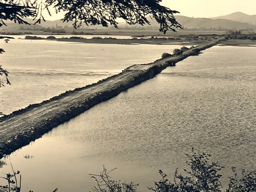 Črnobela fotografija nasipa, ki poteka čez Cerkniško jezero.