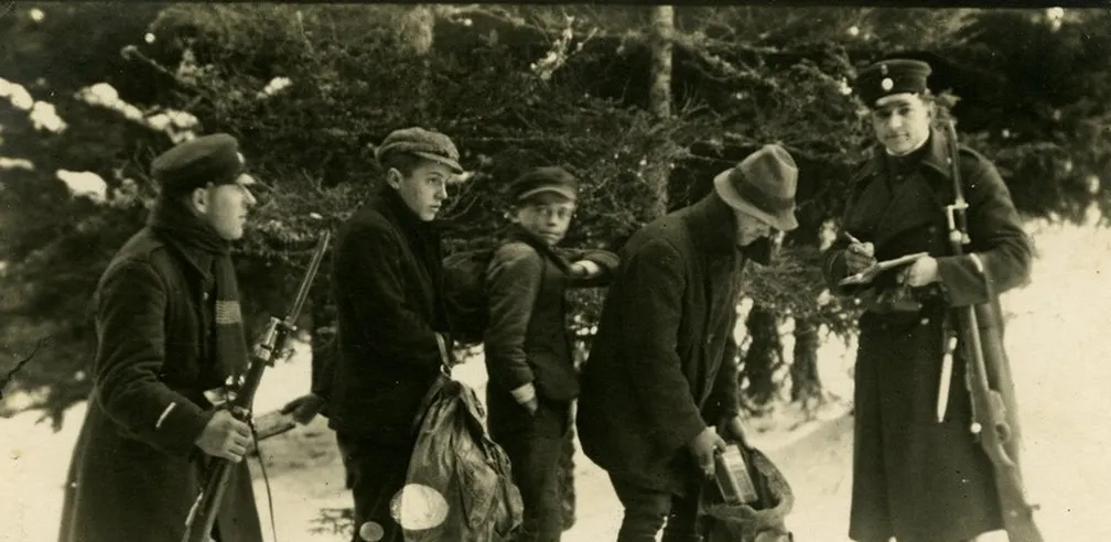 Črnobela fotografija srečanja tihotapcev in obmejnih organov v zasneženih javorniških gozdovih.