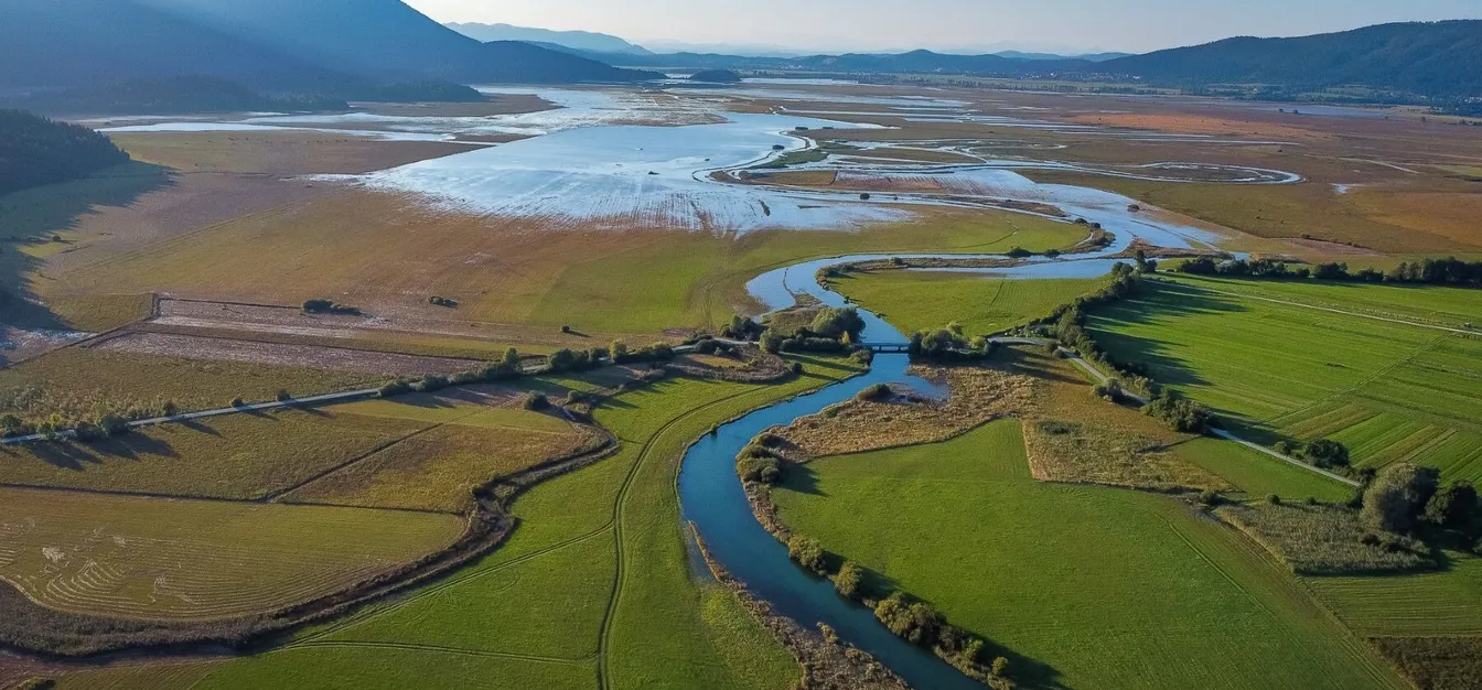 Aerial view of Lake Cerknica with the winding Stržen stream, floodplain meadows and the karst landscape of Notranjski Park.