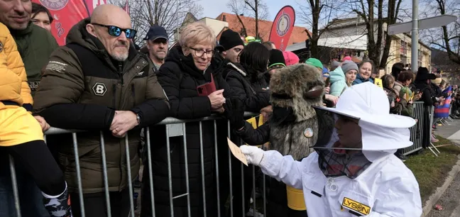 Udeleženec v čebelarski zaščitni obleki deli vrečke s semeni obiskovalcem ob poti.