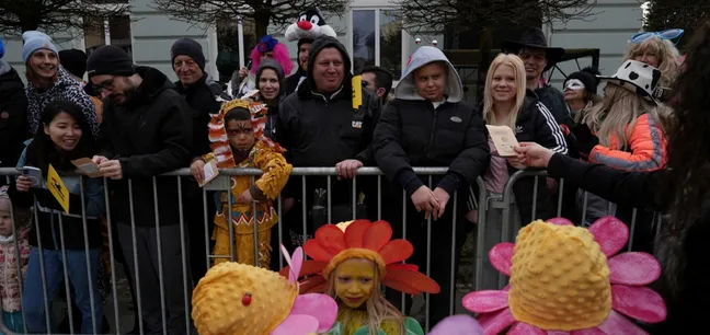 Otroci v cvetličnih pustnih kostumih nastopajo pred občinstvom med pustnim karnevalom v Cerknici.