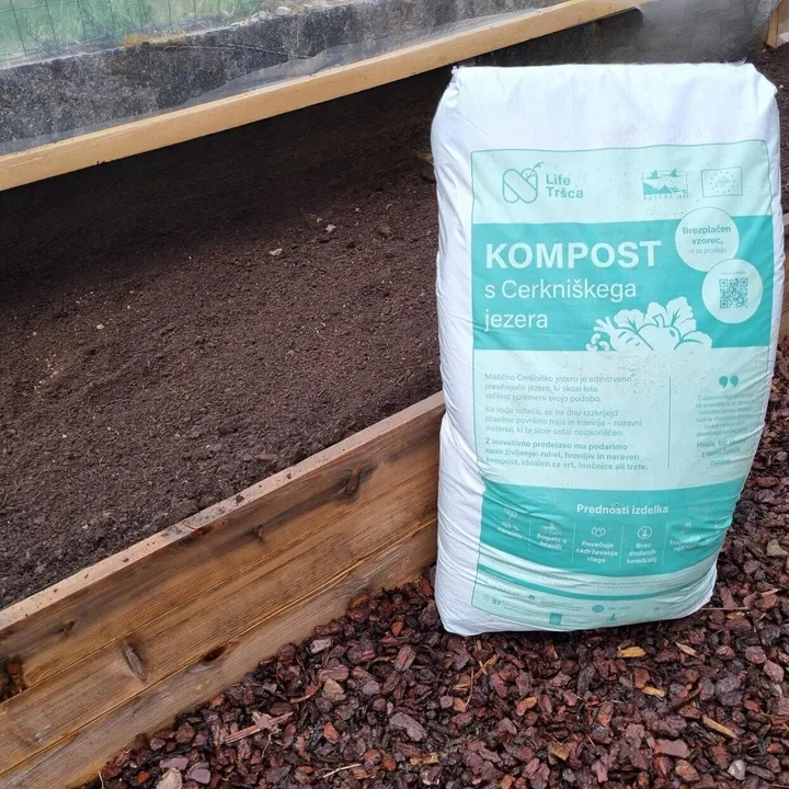 Vreča komposta je postavljena ob dvignjeno gredo, napolnjeno s sveže pogrnjeno plastjo komposta v rastlinjaku.