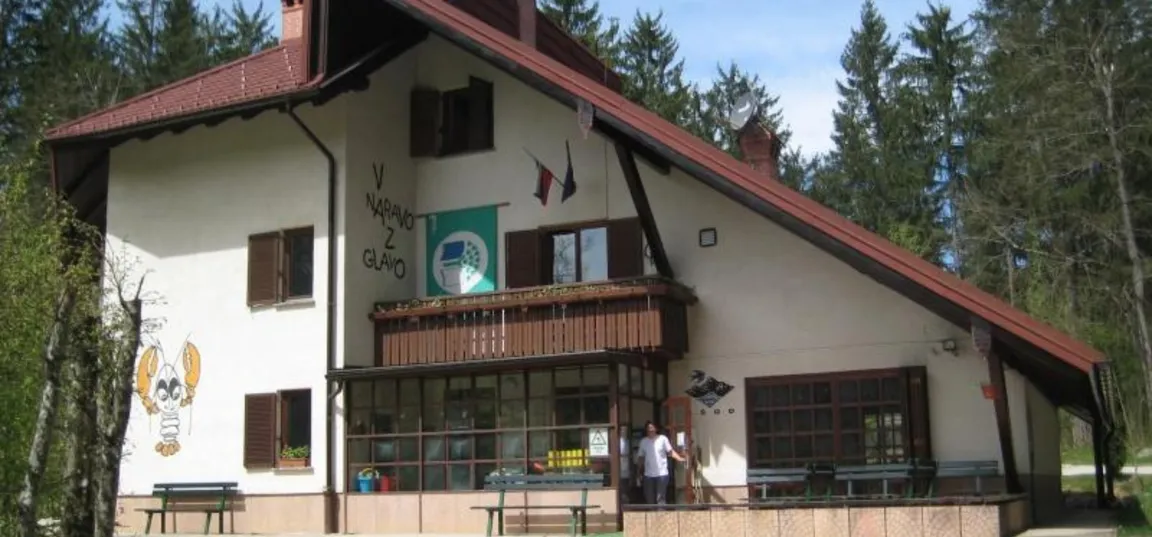 Center za šolske in obšolske dejavnosti Rak v Rakovem Škocjanu-Stavba z napisom in ilustracijo sove, z balkonom, zastavami in zunanjimi mizami.