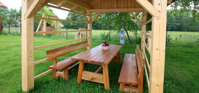 Guesthouse and Pizzeria Pri Stani-Wooden benches and a table under a small barn on a meadow, with an orchard in the background.