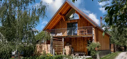 Hiša zdravega oddiha-two-story wooden house with steep roof, balcony with outdoor furniture, and green garden.