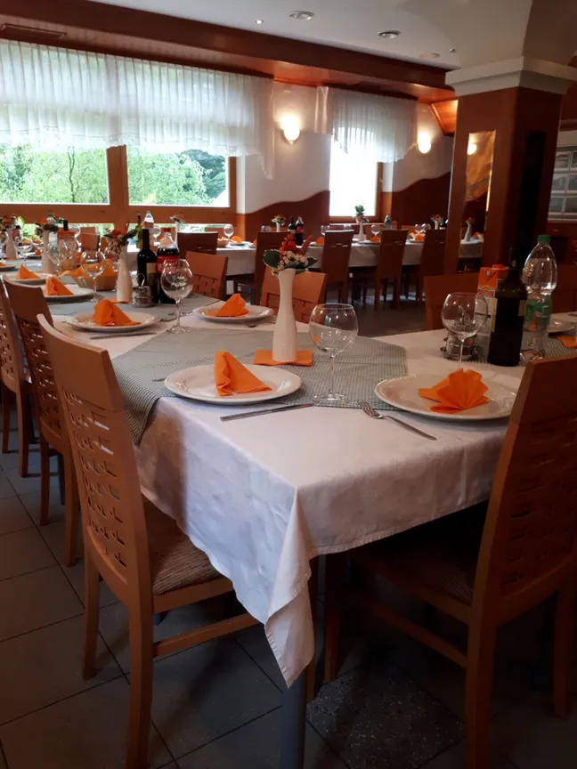 Hotel Rakov Škocjan-Restaurant dining area with tables set with white tablecloths, decorative napkins, flower arrangements, and bottles.