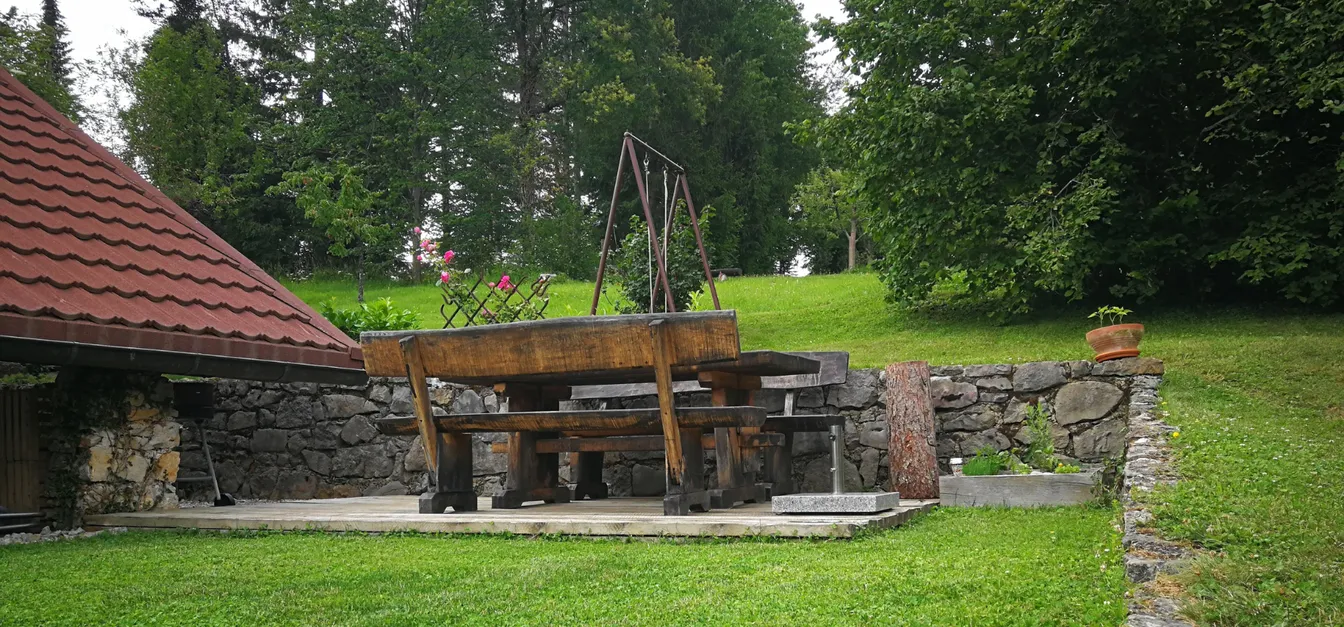 Lake view holiday home-Zunanja terasa s kamnito podlago, leseno mizo in klopmi, obdana z zelenjem in okrasnimi lončnicami.