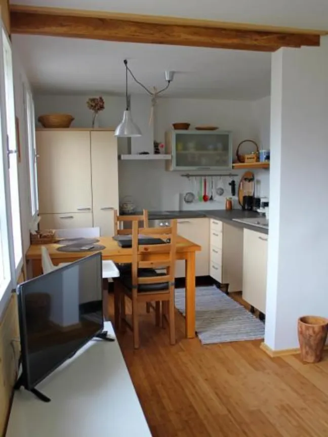 Lake view holiday home-Majhna kuhinja z jedilnim kotom, svetlimi omaricami, lesenim podom in naravno svetlobo, pred kuhinjo pri strani nizka omarica s televizorjem.