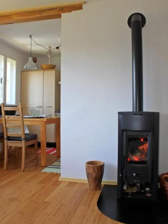 Lake view holiday home-Notranji prostor z moderno črno pečjo na drva, leseno talno oblogo in jedilnim kotom ob velikih oknih.