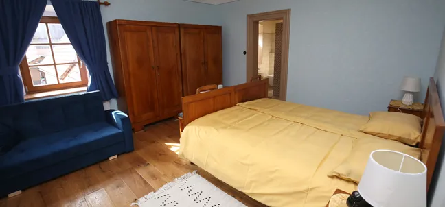 Notranjska hiša-Bedroom with wooden bed and yellow bedding, blue sofa by the window with blue curtains, and wooden wardrobe.