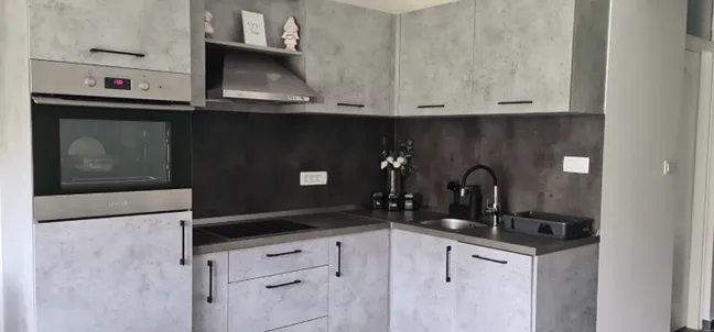 Unec Apartment-Corner kitchen with built-in oven, cooktop, hood and gray cabinets.