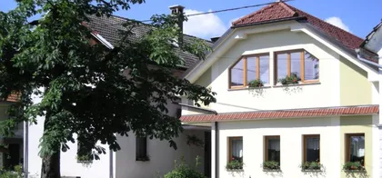 Facade of a house with yellow and white walls and a red roof, surrounded by greenery at Tourist farm Logar.