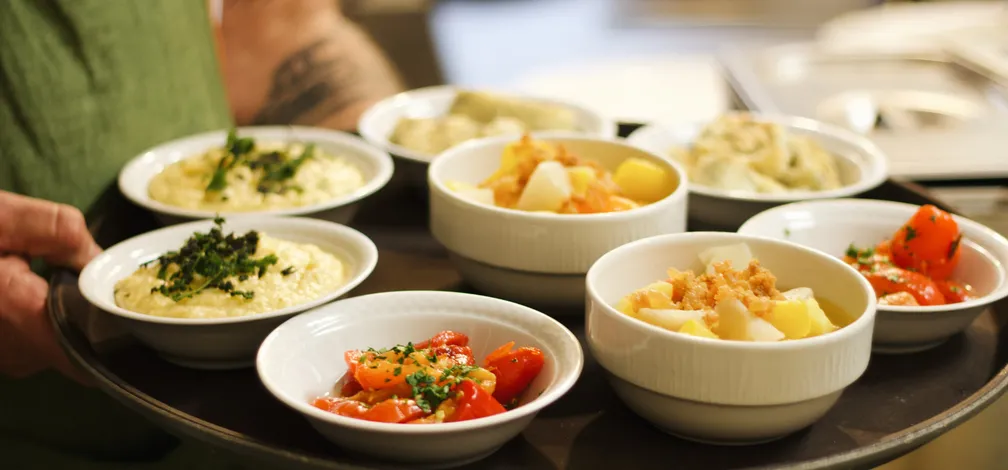 Na pladnju različna paleta jedi v manjših belih skodelicah v gostilni Cajnarje.