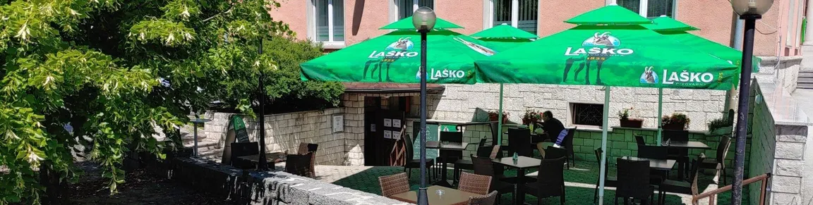 Vrt okrepčevalnice Valvasorjev hram z zelenimi senčniki in nekaj zelenja.