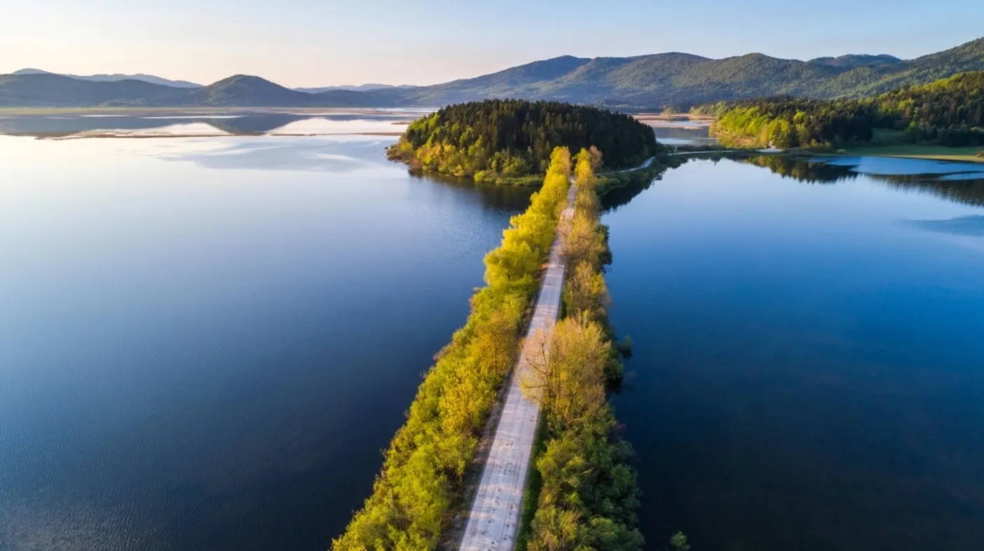 Pogled na polno Cerkniško jezero in nasip, ki vodi čezenj, iz zraka.