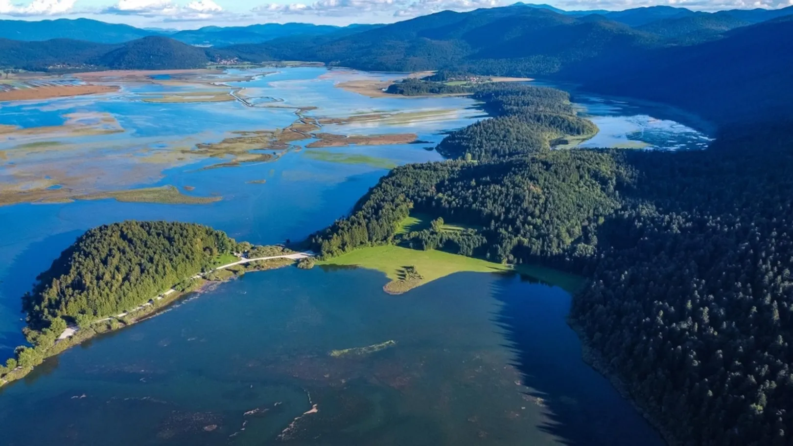 Cerkniško jezero slikano iz zraka s srednje visokim vodostajem, v intenzivno zelenih barvah.